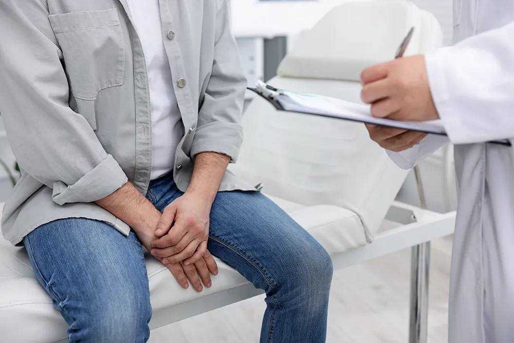 Doctor taking notes during a consultation while a patient sits and discusses their medical concerns.