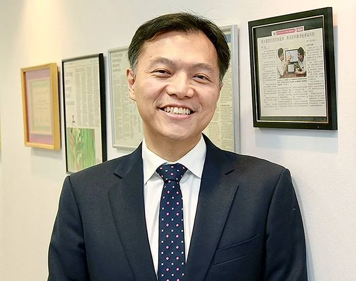 Dr Lincoln Tan, Consultant Urologist in Singapore, standing in his clinic with professional achievements displayed on the wall.