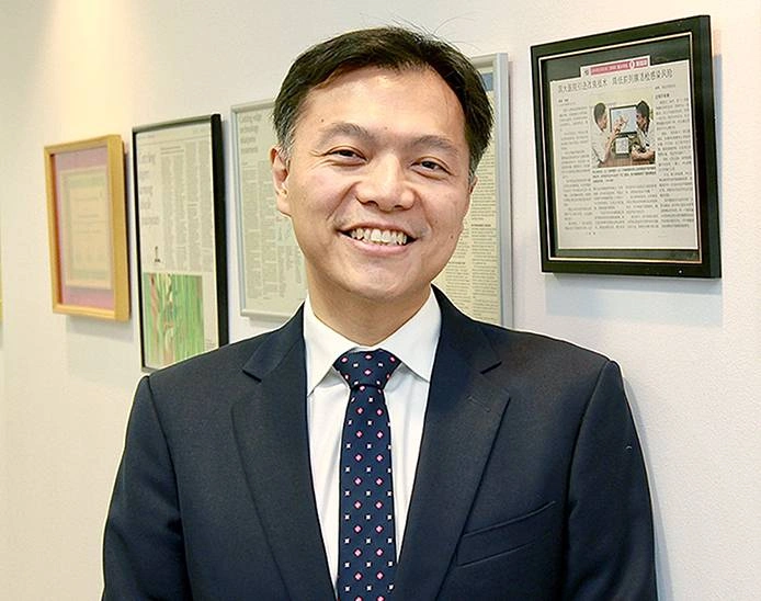 Dr Lincoln Tan, Consultant Urologist in Singapore, standing in his clinic with professional achievements displayed on the wall.